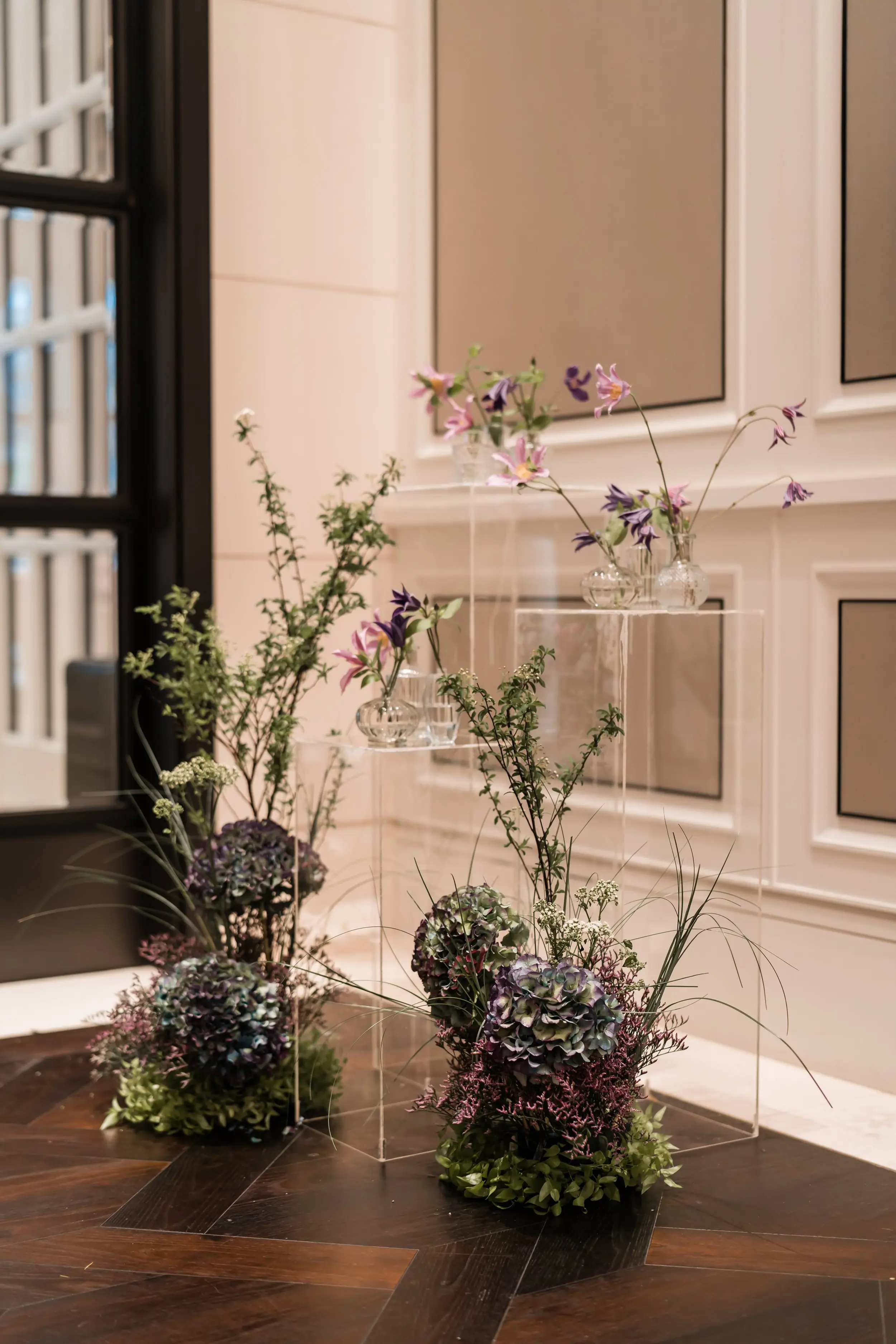 Bud vases placed on clear acrylic plinths to create an interesting and alluring decor alongside curated hedges that are reminiscent of a luxurious garden, befitting of Caroline’s Mansion.